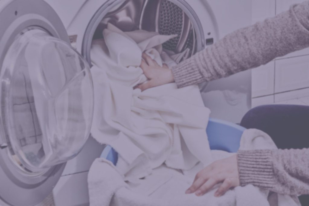 Hands pulling white sheets out of a dryer.